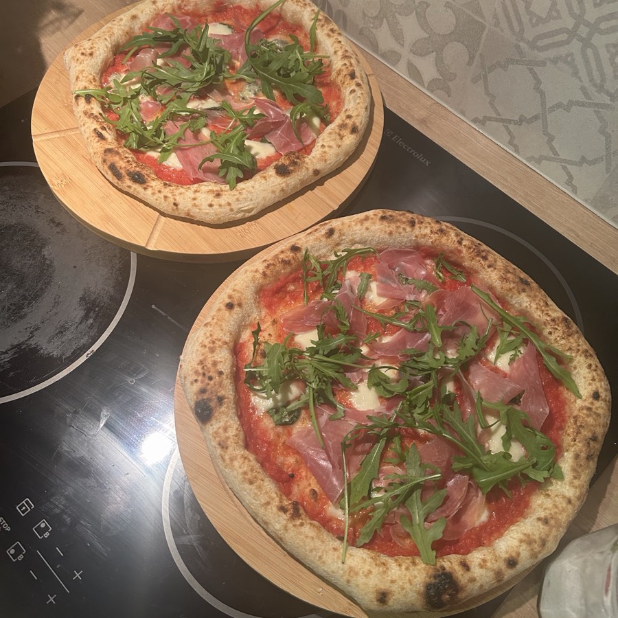 Dwie pizze z prosciutto i rukolą, świeżo po wypieku, na drewnianych deskach